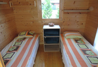 Two single beds with floral-striped bedding in a cozy wooden cabin room in Germany, window view.