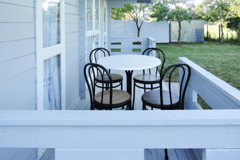 White-painted porch with a round table and four chairs beside a cabin, overlooking a green garden.