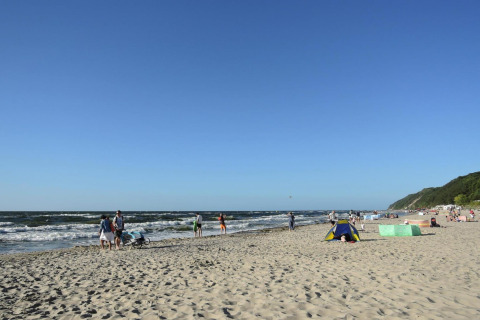 People enjoying a sunny day at a sandy beach in Germany with blue skies, waves, and green hills nearby.
