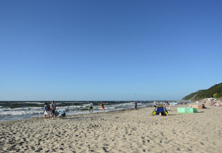 People enjoying a sunny day at a sandy beach in Germany with blue skies, waves, and green hills nearby.