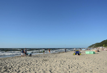 Personas disfrutan de un día soleado en una playa de arena en Alemania con cielo azul y colinas verdes.