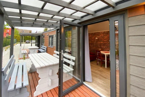 Åben terrasse med træborde og bænke foran bungalower, med udsigt til indendørs spisestue, i Dziwnow.