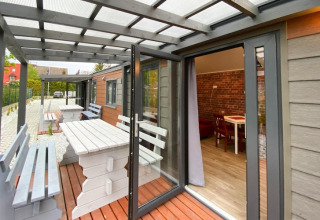Overdekt terras met witte houten banken en tafels bij bungalows, open deur naar woonkamer, in Dziwnow.