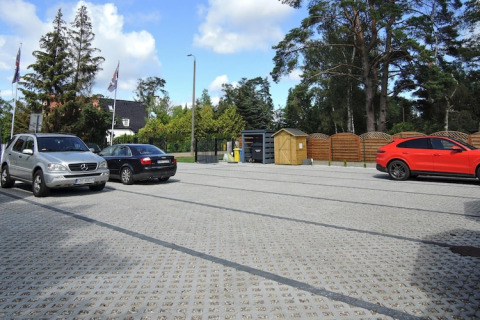 Parking bij Bungalows Pirates in Dziwnow met auto's, houten omheining en veel bomen rondom.