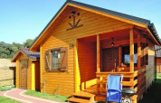 Houten chalet op vakantiepark Wiselka met veranda, barbecue en stoel in Duitsland onder een blauwe lucht.