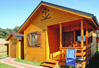 Houten chalet op vakantiepark Wiselka met veranda, barbecue en stoel in Duitsland onder een blauwe lucht.