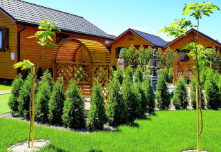 Holiday resort with pool Wiselka-35 sqm Type A in Germany, manicured garden, wooden chalets, and hedges.