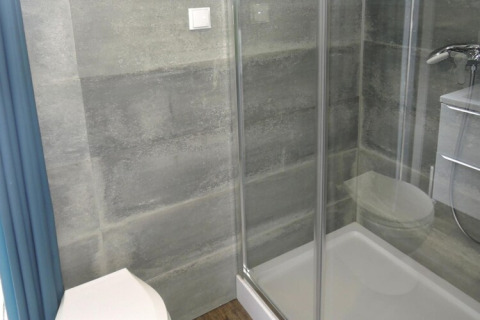 Moderne badkamer met glazen douche, toilet en grijze tegels bij Bungalows Pirates in Dziwnow.