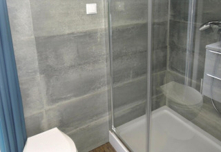 Moderne badkamer met glazen douche, toilet en grijze tegels bij Bungalows Pirates in Dziwnow.