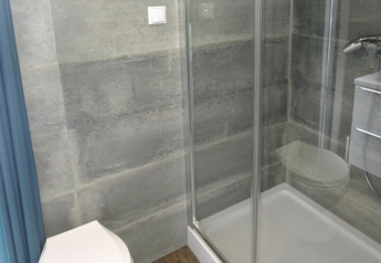 Salle de bain moderne avec cabine de douche en verre, toilettes et carrelage gris à Bungalows Pirates.