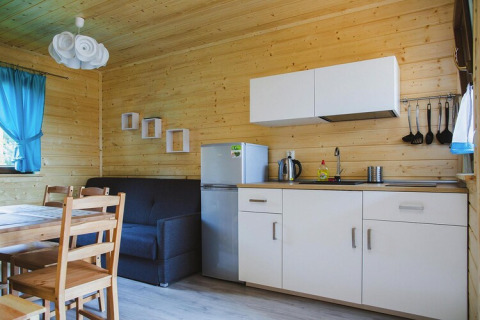 Cozy kitchenette and living area with wooden walls, dining table, sofa, and modern white kitchen cabinets.