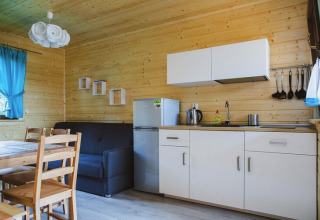 Hyggeligt køkken og stueområde i træ med spisebord, sofa, hvidt køkken og blå gardiner i et feriehus.