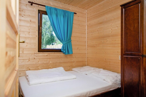 Cozy wooden bedroom with double bed, blue curtain, window, and wardrobe at Wiselka holiday resort in Germany.