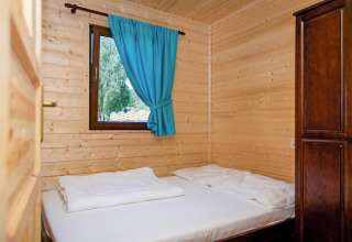 Camera in legno con letto matrimoniale, tendaggio blu e armadio presso il resort Wiselka in Germania.