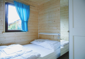 Heldere slaapkamer met houten muren, blauw gordijn, tweepersoonsbed en spiegelkast in Duits vakantieverblijf.