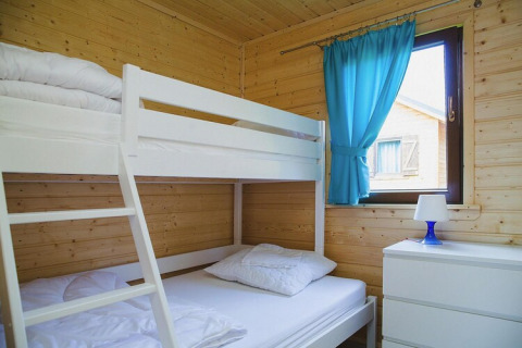 Lichte slaapkamer met wit stapelbed, houten muren, blauwe gordijnen en commode in Wiselka.