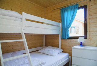 Bright room with white bunk bed, wooden walls, blue curtains, and dresser at Holiday resort Wiselka.