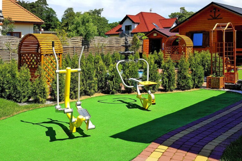 Area fitness all'aperto con gazebo in legno, prato artificiale e attrezzi ginnici presso un resort tedesco.