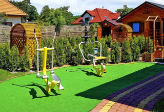 Buiten fitness met houten prieeltjes, kunstgras en fitnesstoestellen aan een vakantiehuis in Duitsland.