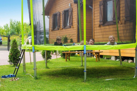 Children playing on a trampoline outside a wooden lodge at Holiday resort with the pool Wiselka-35 sqm Type A in Germany.