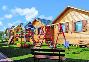 Vakantieverblijf met houten chalets en speeltuin, schommels, bankjes en gras bij mooi weer.