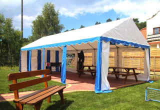 Outdoor marquee with blue and white stripes, benches and picnic tables at Wiselka holiday resort, Germany.