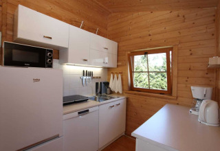 Moderne houten keuken in vakantiehuis in Miedzyzdroje met witte kasten, raam en keukenapparatuur.