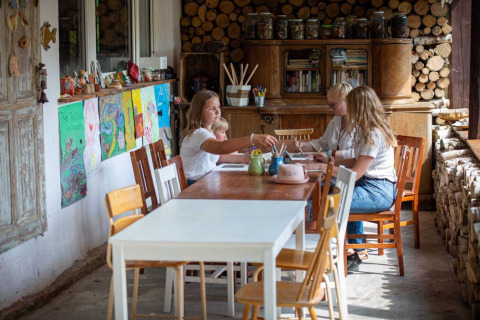 Vier mensen zitten aan een tafel te knutselen in een gezellige lodge met houtstapels en kindertekeningen.