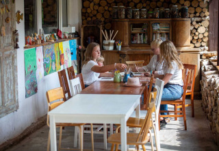 Fire personer sidder ved et bord og laver kunsthåndværk i en hyggelig lodge med træstabler og malerier.