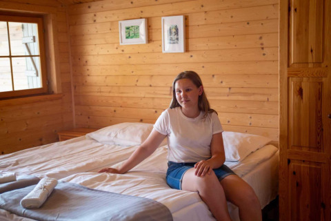 Woman sitting on a bed in a wooden room at the lodge 'Holiday homes in Miedzyzdroje' in Germany.