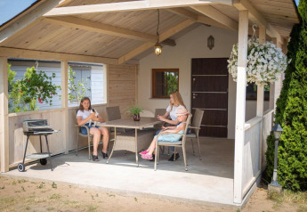 Famille assise sur la terrasse couverte d’une maison de vacances à Miedzyzdroje, Pologne, avec fleurs et verdure.
