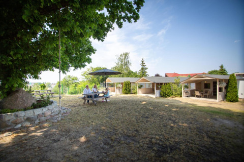 Outdoor area at holiday homes in Miedzyzdroje with table, umbrella, and four people, surrounded by trees and cabins.