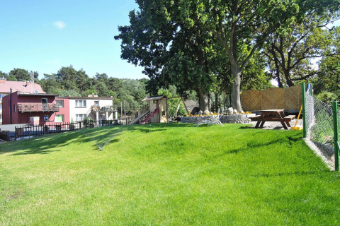 Groen gazon en speeltuin aan Holiday homes te Międzyzdroje, met bomen en een picknicktafel buiten.