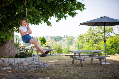 Vrouw op schommel bij picknicktafels en parasol, Holiday homes in Miedzyzdroje, Duitsland.