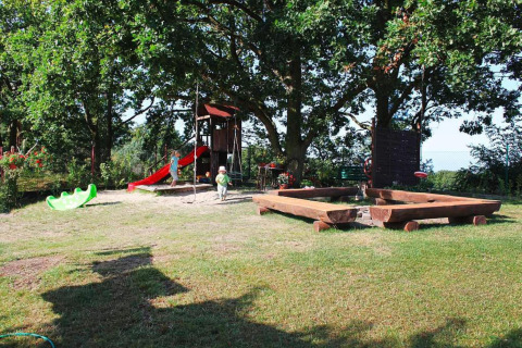 Speeltuin met glijbaan, zandbak en kinderen onder bomen bij vakantiehuizen in Miedzyzdroje, Duitsland.