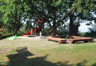 Speeltuin met glijbaan, zandbak en kinderen onder bomen bij vakantiehuizen in Miedzyzdroje, Duitsland.