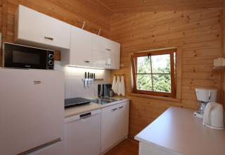Modern small cabin kitchen with white cabinets, appliances, wooden walls, and a window viewpoint.
