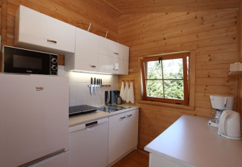Cocina pequeña y moderna de cabaña con gabinetes blancos, electrodomésticos y paredes de madera.