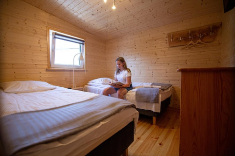 Vrouw leest op een bed in een gezellige, houten vakantiewoning met twee eenpersoonsbedden en raam.