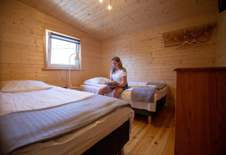 Vrouw leest op een bed in een gezellige, houten vakantiewoning met twee eenpersoonsbedden en raam.
