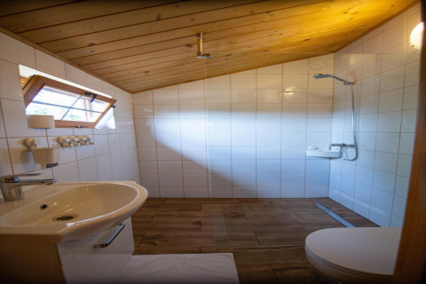 Badezimmer im Ferienhaus in Miedzyzdroje, schräges Holzdeck, Dusche, Waschbecken und Fenster.