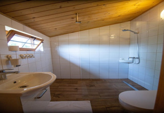 Badkamer in een chalet met schuin houten plafond, witte tegels, douche en lavabo in Miedzyzdroje, Duitsland.