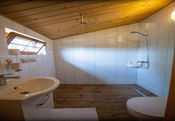 Baño en cabaña con techo inclinado de madera, azulejos blancos, ducha y lavabo en Miedzyzdroje, Alemania.
