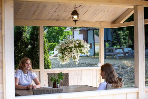 Twee vrouwen zitten in een houten huisje met hangbloemen bij Holiday homes in Miedzyzdroje, Duitsland.