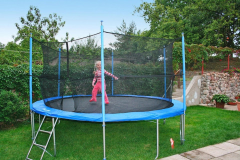 Een kind speelt op een grote trampoline met veiligheidsnet in de tuin van een vakantiehuis.
