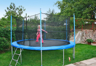 Een kind speelt op een grote trampoline met veiligheidsnet in de tuin van een vakantiehuis.