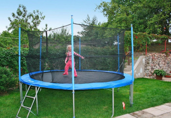 Niña jugando en una gran cama elástica con red de seguridad en el jardín de una casa de vacaciones.