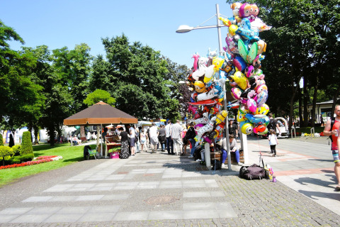 People gather in a park near Holiday homes in Miedzyzdroje, Germany, with balloon stands and vendors.
