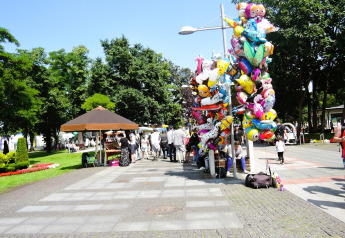People gather in a park near Holiday homes in Miedzyzdroje, Germany, with balloon stands and vendors.