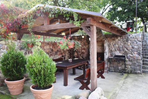Overdekt stenen terras met houten tafel, banken, planten en barbecue bij vakantiehuis in Miedzyzdroje, Duitsland.